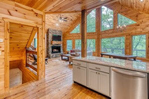 L’intérieur d’un chalet en bois est doté d’une cheminée en pierre, de planchers en bois et de grandes fenêtres qui offrent une vue sur l’extérieur.