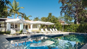A swimming pool with lounge chairs and umbrellas, surrounded by trees and a building.