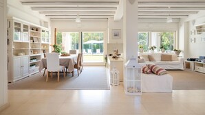 A spacious living area with a dining table, white furniture, and a view to the outside.