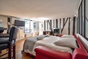 Habitació d'hotel moderna amb un llit gran, una taula de treball amb una cadira, una televisió i una finestra amb persianes.