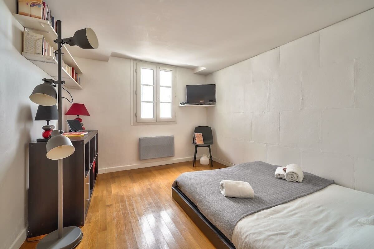 Une chambre à coucher avec un lit, une table de chevet, une lampe et un téléviseur fixé au mur.