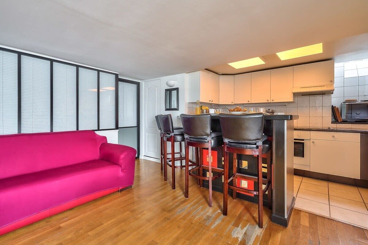 A modern kitchen with a bar area, wooden flooring, and a bright window.