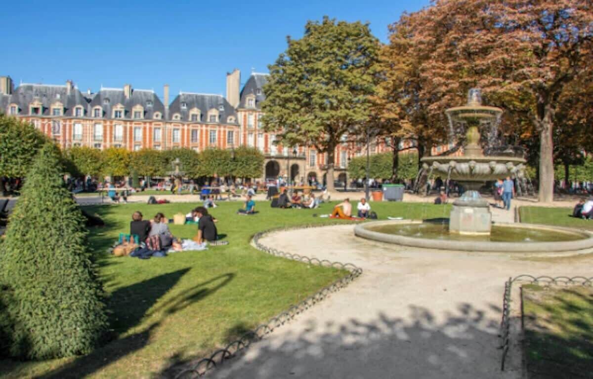 Un parc avec une fontaine, des gens assis sur l’herbe et un bâtiment en arrière-plan.