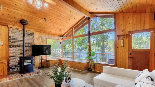 A cozy cabin interior with a fireplace, wooden walls, large windows, a sofa, and a table with a plant. - Lake access cabin near trails and spring (Black Diamond)