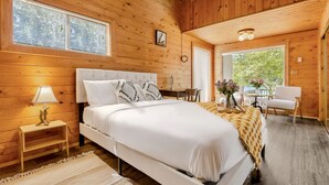 A wooden cabin bedroom with a bed, bedside table, lamp, and a view of the outdoors. - Lake access cabin near trails and spring (Black Diamond)