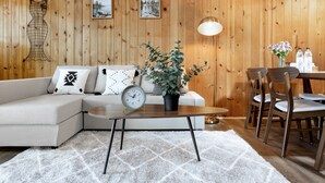 A cozy room with a wooden wall, a sofa with patterned cushions, a small table with a clock, a potted plant, and a dining area with chairs. - Lake access cabin near trails and spring (Black Diamond)