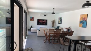 Un salon moderne avec un canapé, une table à manger et des chaises. Un téléviseur est fixé au mur et une fenêtre laisse entrer la lumière naturelle.