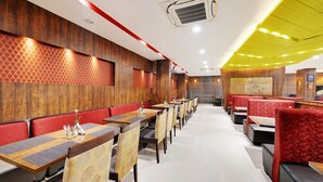 A restaurant with wooden panel walls, red cushioned booths, and a long counter with tables and chairs. - La Sara Gateway (Anekal)