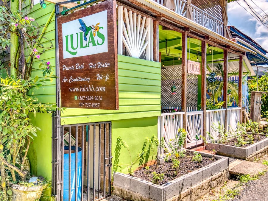 A green building with a sign advertising LULAS services, including private bath, hot water, air conditioning, and Wi-Fi.
