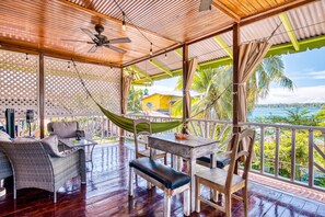 A covered outdoor seating area with wicker furniture, a hammock, and a view of the ocean and palm trees. - Lula's Bed & Breakfast (Bocas del Toro)