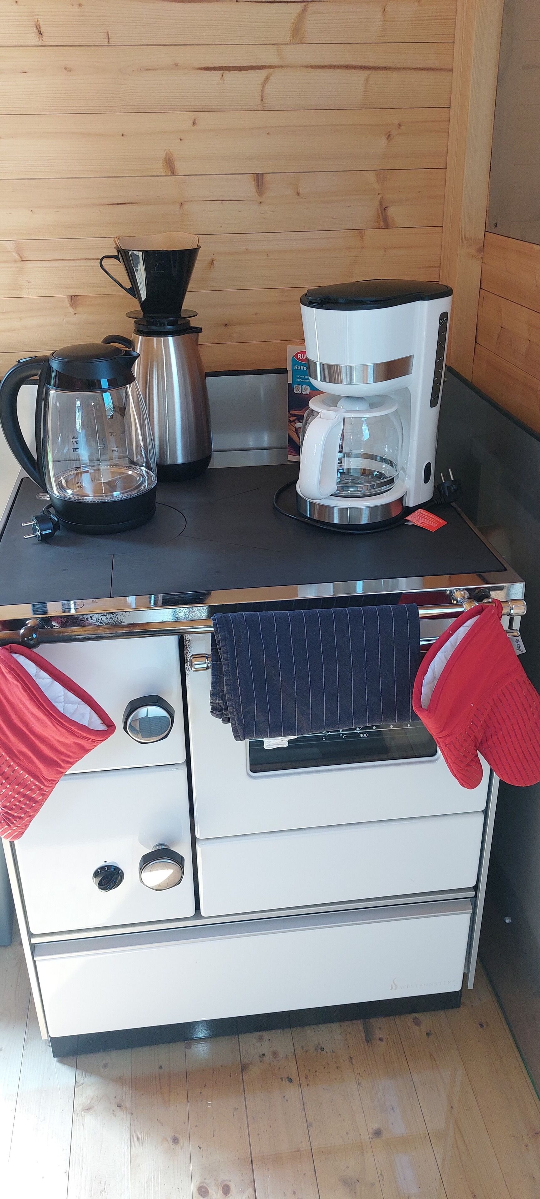 A kitchenette with a stove, coffee maker, and kettle.