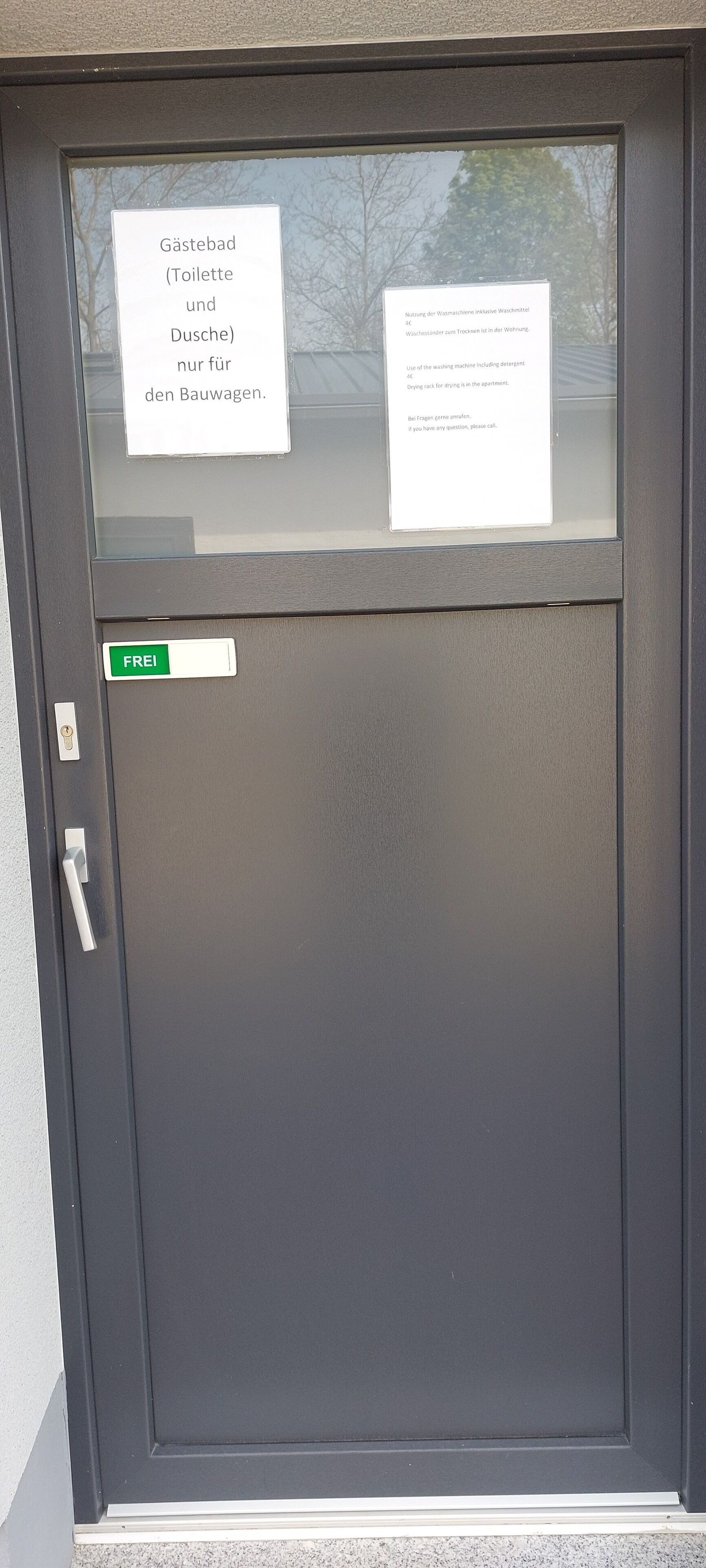 Une porte portant l’inscription « Frei », qui indique qu’il s’agit d’une entrée libre, et deux panneaux d’information en allemand concernant l’utilisation des machines à laver et des étendoirs dans l’appartement.