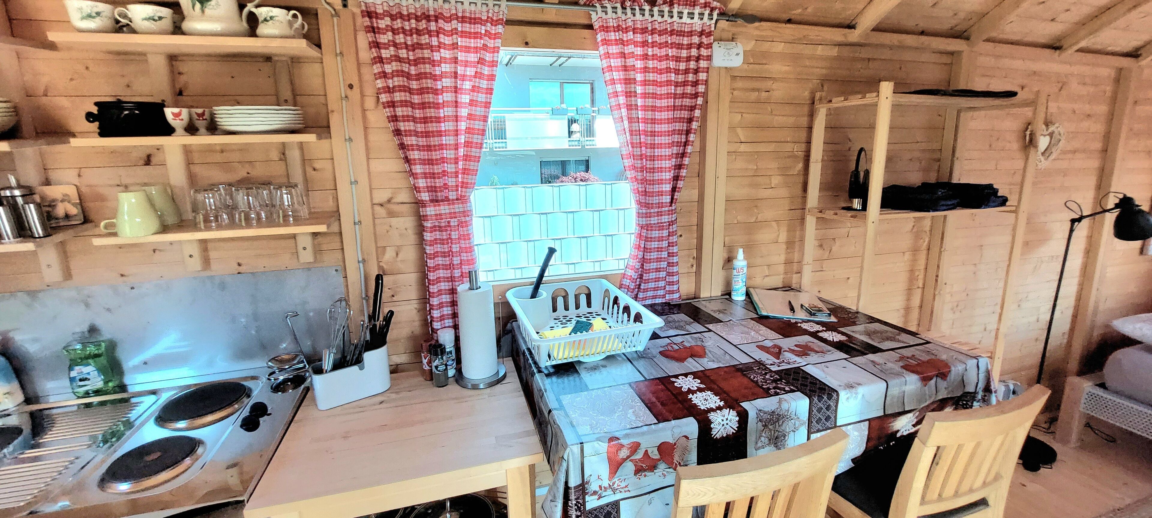 Een landelijke keuken met houten planken, een tafel met een quiltkleed en een raam met rood-wit geruit gordijnen.
