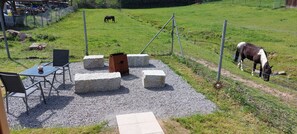Un espace patio avec une table et des chaises, entouré de blocs de pierre, et un champ clôturé où se trouvent des chevaux.