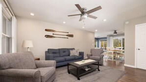 Ein Wohnzimmer mit blauem Sofa, zwei Sesseln, einem Couchtisch und einem Deckenventilator.