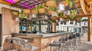 Eine Bar mit einer langen Theke, mehreren Barhocker, hängenden Pflanzen und einem modernen Deckenstil.