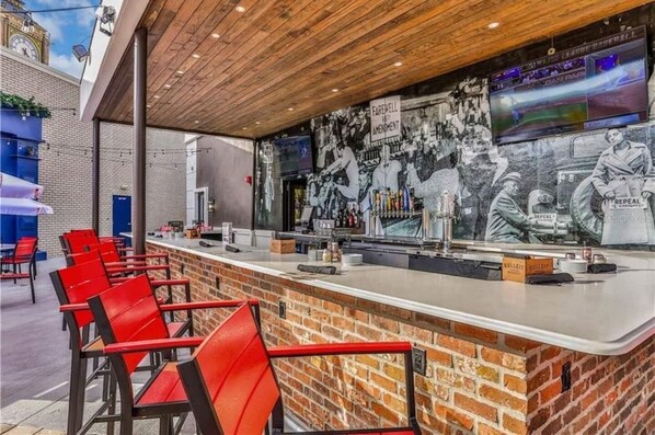 A bar with a brick counter, red chairs, and a mural depicting historical figures and events.
