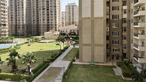 A high-rise residential building with multiple balconies, a central courtyard with palm trees, and a playground. - Luxury studio (Noida)