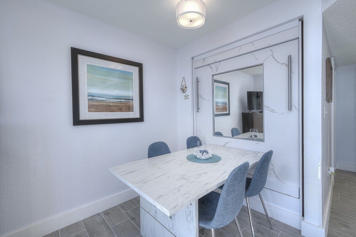 A dining area with a white marble table and blue chairs, a framed picture on the wall, and a door with a mirror.