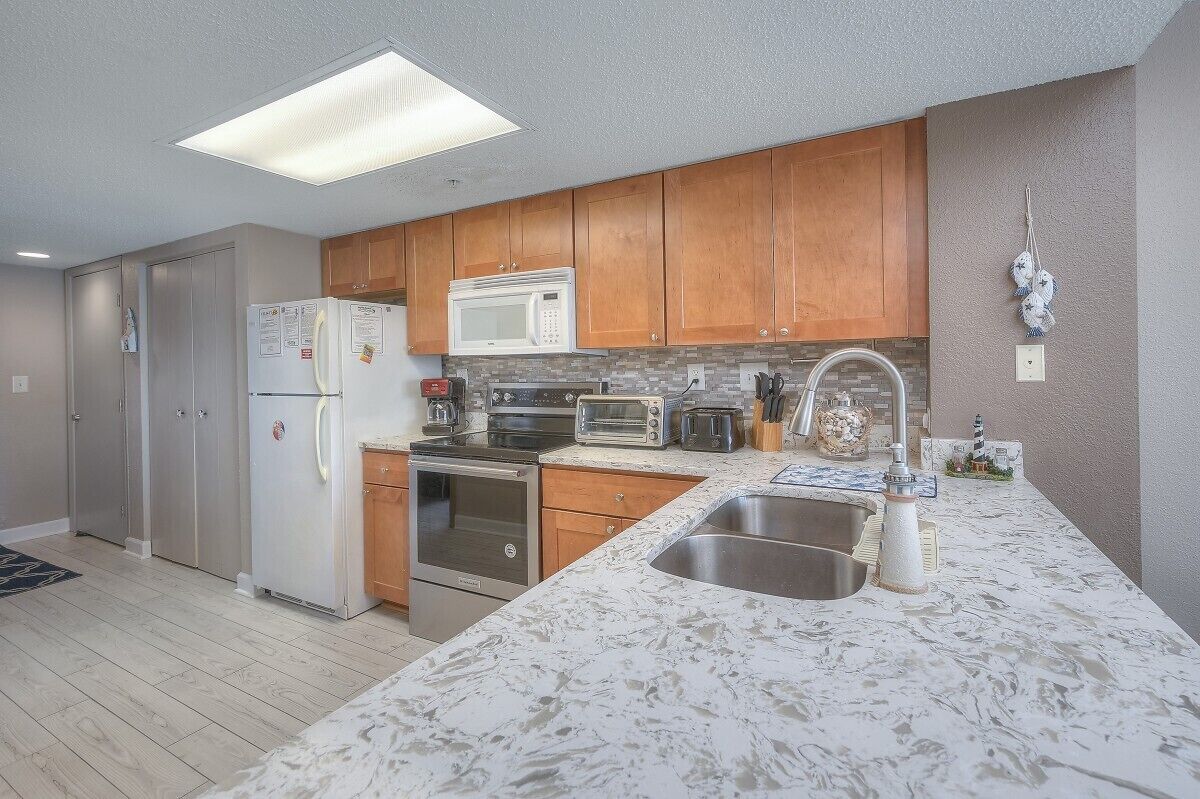 A modern kitchen with wooden cabinets, stainless steel appliances, and a marble countertop.