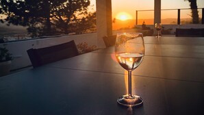 A glass of white wine on a table with a sunset view through a covered outdoor area. - Villa with fabulous views, pool, pool table, table tennis table, 15mins to beach (Amoreira, Obidos)