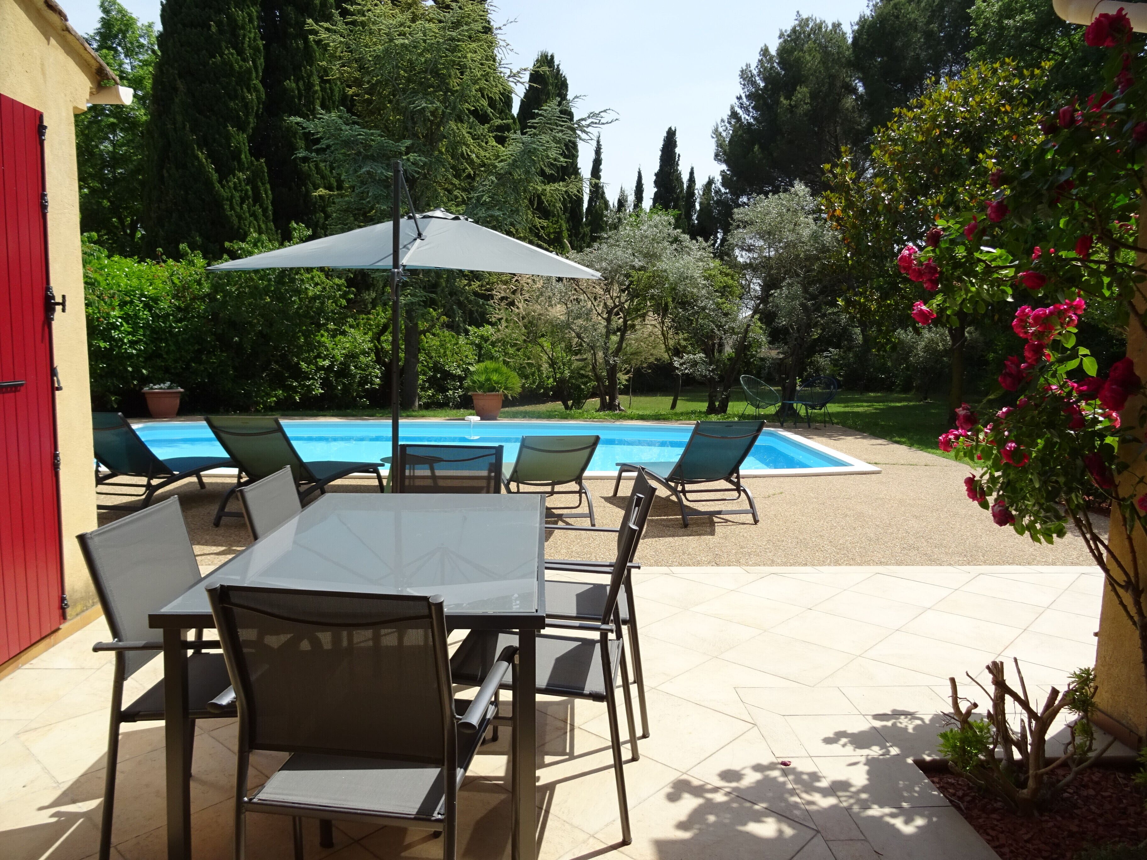 A poolside area with a table and chairs, a pool, and surrounding greenery.