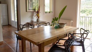 A dining area with a wooden table, black chairs, and a vase with plants. - Villa de Vacance 6 Personnes (Orpierre)
