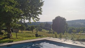 A clear swimming pool with a tiled edge, surrounded by a grassy area and trees.