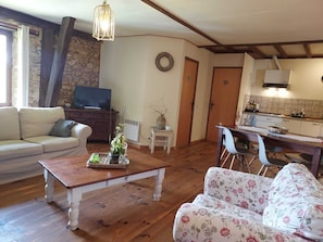 Un salon chaleureux avec une table basse en bois, un canapé à motifs floraux, un téléviseur et un coin cuisine comprenant une table à manger et des chaises.