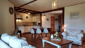 A cozy living room with a sofa, a coffee table, and a floral-patterned armchair. There is a kitchen area with a dining table and chairs.