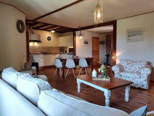 Un salon chaleureux avec un canapé, une table basse et un fauteuil à motifs floraux. Il y a également un coin cuisine avec une table à manger et des chaises.