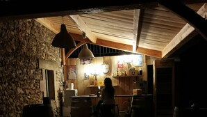 A dimly lit wooden interior with a stone wall, a bar area, and a person standing near the bar.