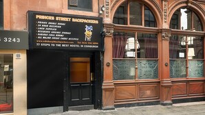 Un edificio con un cartel que indica 'Princes Street Backpackers', mencionando servicios como habitaciones privadas, recepción las 24 horas y almacenamiento de equipaje.