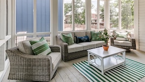 Ein Wintergarten mit Korbmöbeln, einem weißen Couchtisch und großen Fenstern.