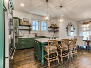 A kitchen with green cabinets, a central island, and a dining area with wicker chairs. - Carlton Landing-Wild Horses (Carlton Landing)