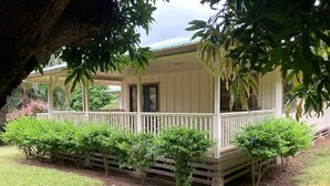 Une véranda couverte avec une balustrade en bois, entourée d’arbustes soigneusement taillés et d’une pelouse bien entretenue.