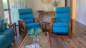 Un salon moderne avec une table basse en verre, deux fauteuils bleus et une table d’appoint en bois.