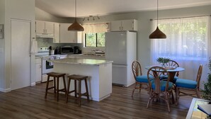 Une cuisine moderne avec des meubles blancs, un îlot central et un coin repas doté de chaises et d’une table en osier.