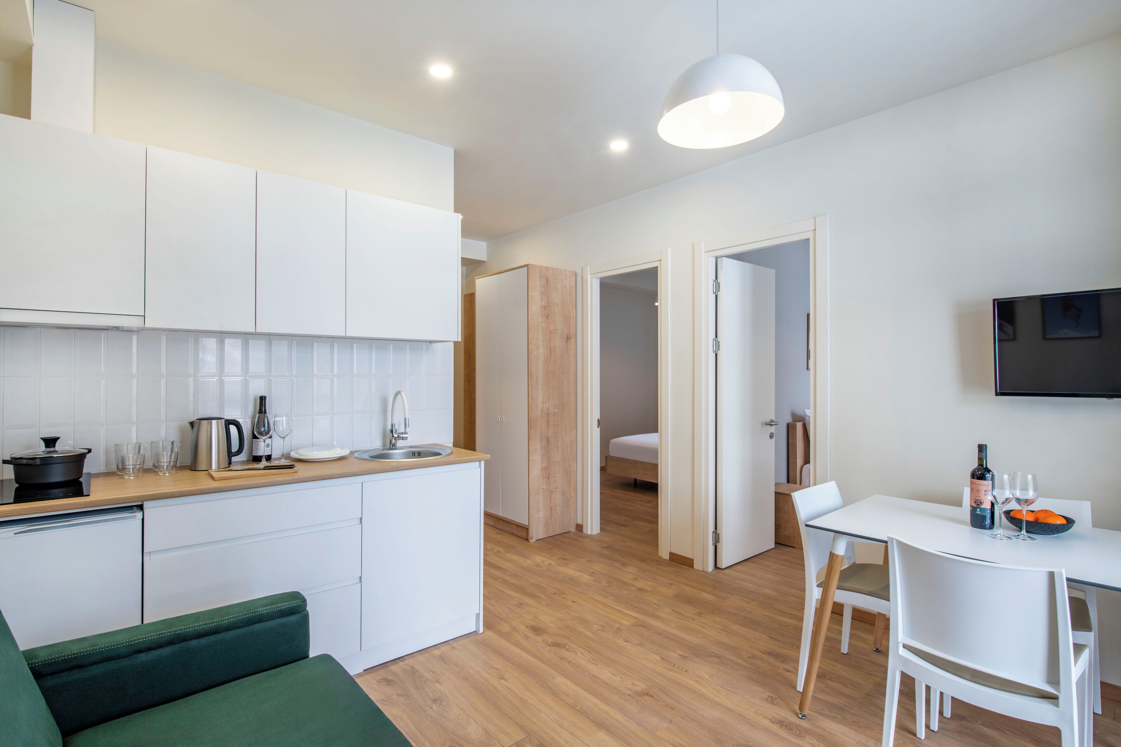 Una cocina moderna con armarios blancos, encimera de madera y comedor con mesa y sillas blancas.