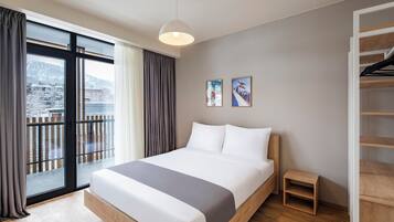Ein modernes Hotelzimmer mit einem großen Bett, einem kleinen Nachttisch, einem Kleiderschrank und einem Balkon mit Blick auf eine verschneite Landschaft.