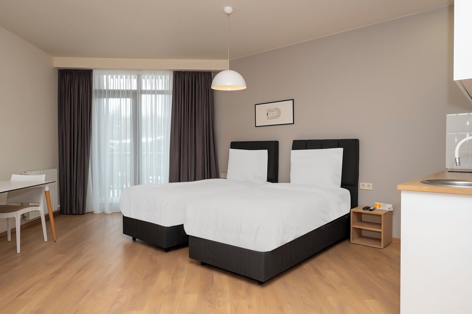 A hotel room with two beds, a desk, and a kitchenette.