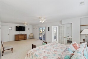 Une chambre à coucher comprenant un lit, une commode, un téléviseur, un ventilateur de plafond et une porte donnant sur un balcon.