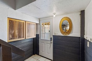 Un couloir avec une porte en bois, une porte blanche dotée d’un panneau de verre et un miroir fixé au mur.