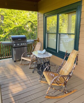 Una terraza techada al aire libre con una parrilla, sillas mecedoras de mimbre y una mesa.
