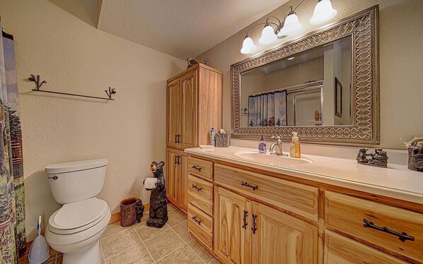 Un baño con inodoro, armarios de madera, tocador con espejo y lavamanos.