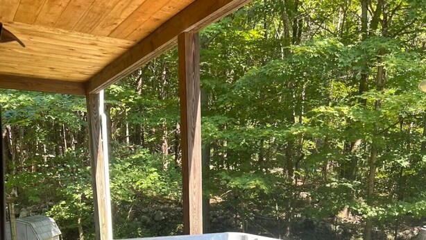 Un bain à remous situé dans un espace boisé, avec une terrasse en bois et un mur de pierres en arrière-plan.