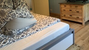Een slaapkamer met een bed, een houten dressoir, een televisie en een bijzondere, bolvormige plafondlamp.