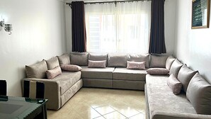 Una sala de estar con un sofá modular, una mesa de centro de vidrio y una ventana con cortinas.