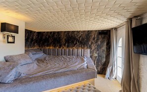 A modern bedroom with a marble wall, a tufted headboard, and a flat-screen TV.