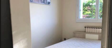 A bedroom with a single bed, a radiator, a window with a view of greenery, and a wall-mounted sign.